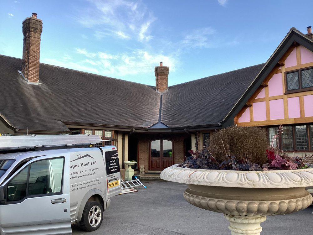 White van parked outside a large house with a dark pitched roof and stone planter