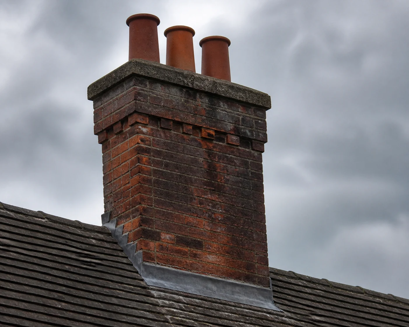 Cracked chimney pointing above a rain-darkened tiled roof